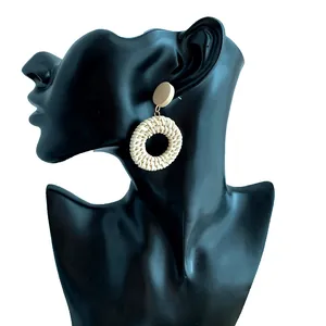 Close-up of handmade woven rattan earrings with a light brown stud on a black model