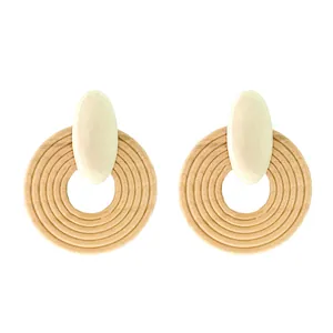 Detail shot of round wooden drop earrings with circular woven texture and beige oval studs