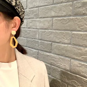Close-up of geometric earrings with beige studs and yellow asymmetric resin charms