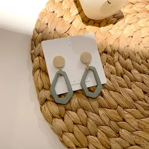 Detail view of geometric wooden earrings with Morandi green pendants on a woven mat