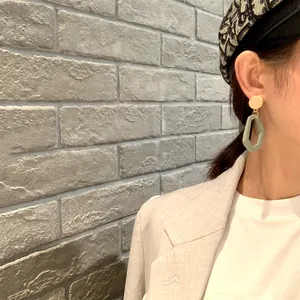 Close-up of geometric green wooden drop earring worn by model in chic beige blazer