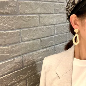 Detail of geometric wooden drop earring in beige on model with light grey background