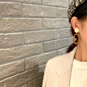 Detail view of model wearing geometric drop earrings with cream studs and brown pendants