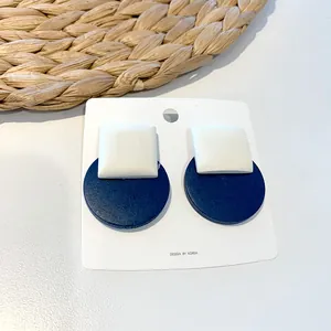 Detail of geometric square and round stud earrings on a white professional card