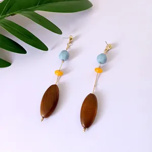 Pendientes largos de acrílico y madera con botones dorados sobre fondo de hojas