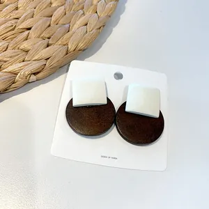 Detail of geometric wood earrings featuring white square and dark brown round studs