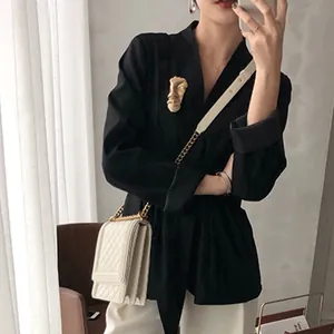 Artistic gold face mask brooch pinned on a black tailored blazer lapel for elegant styling