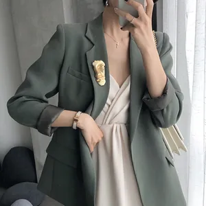 Matte gold face brooch pin for women on a dark green suit jacket with lapel detail