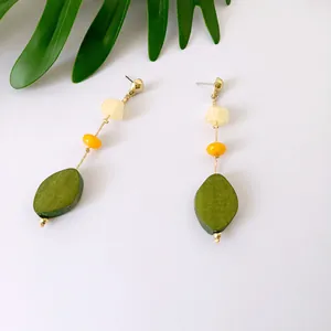 Detalle de pendientes de borla larga con cuentas doradas y colgantes de hoja verde