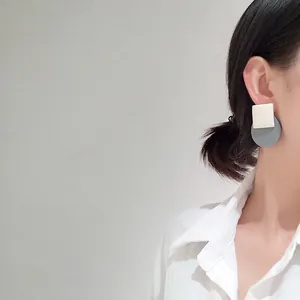 Detail of minimalist geometric white and blue earrings worn by model on white shirt