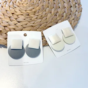Detail view of wooden geometric square and round drop earrings on a white display card