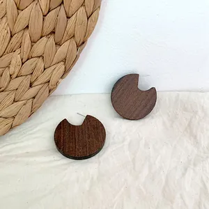 Detailed view of round dark wood earrings with crescent notch on a soft linen background