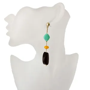 Detalle de pendientes largos geométricos con cuentas de resina turquesa y negra en modelo