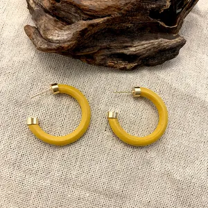 Retro C-shaped wooden hoop earrings in mustard yellow with gold ends on linen background