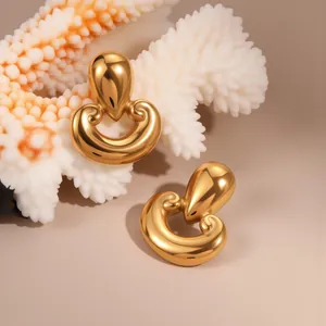 Detalle de pendientes de gota dorados con motivos de volutas sobre un fondo de coral