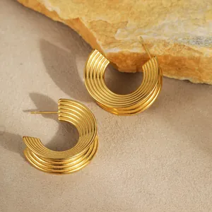 Detalle de los pendientes en C dorados con textura acanalada sobre piedra