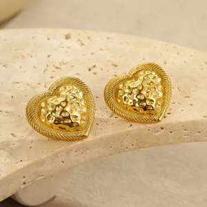 Detalle de pendientes de corazón dorados con textura martillada y borde trenzado en piedra