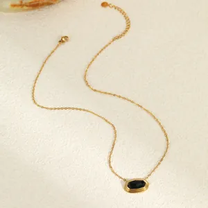 Detail van geometrische zwarte agaat hanger met 18K vergulde ketting op steen