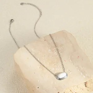 Detail van zilveren ketting met ovale witte hanger rustend op een beige natuursteen
