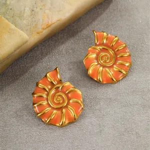 Golden seashell stud earrings with bright orange enamel finish on stone background