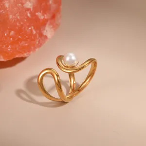 Detailansicht eines wellenförmigen 18K Goldrings mit weißer Perle auf schlichtem Grund