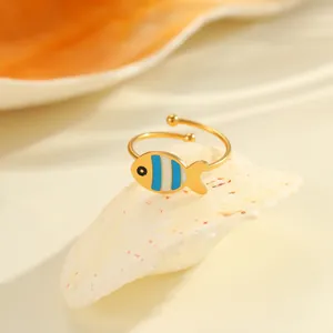 Detail eines verstellbaren Goldrings mit blau-weiß gestreiftem Fisch-Anhänger auf Muschel