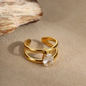 Detail eines 18K vergoldeten Doppelrings mit ovalem Zirkonstein auf sandigem Hintergrund