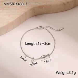 Detail of stainless steel bracelet featuring fish and zircon charms on marble background