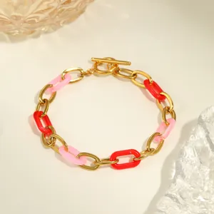 Détail d'un bracelet doré avec maillons en résine rose et rouge et fermoir barre en T