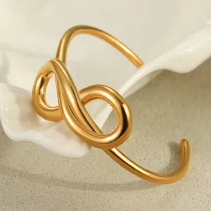 Detailed close-up of 18K gold-plated infinity knot stainless steel bangle on white tray