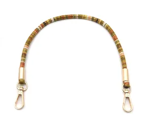 Close-up of ethnic style woven bag strap with golden lobster clasps and green textures
