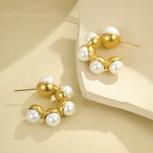 Macro detail of C-shaped gold earrings with five inlaid pearls on a textured stone
