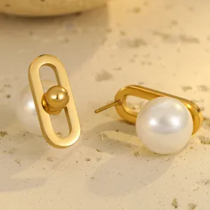 Minimalist gold oval earrings with pearl drop and metal sphere on stone background