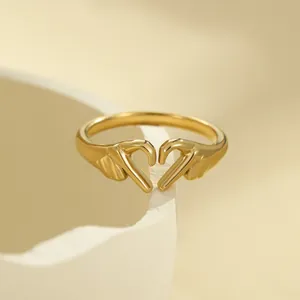 Adjustable golden open ring featuring hands forming a heart shape on warm background