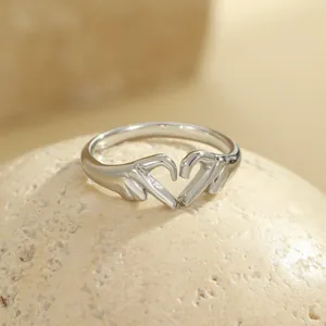 Polished silver heart hand-gesture open ring on a minimalist stone display stand