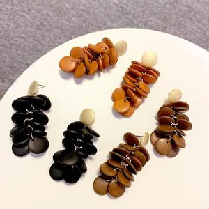 Detail showing layered round wooden disk drop earrings in black, brown, and orange colors