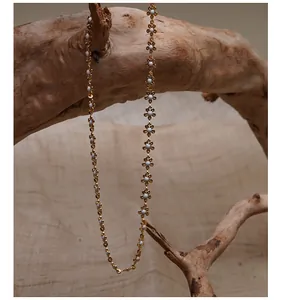 Elegante goldene Metall-Blumenkette mit weißen Blütenblättern auf rustikalem Holzzweig