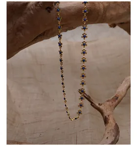 Elegante goldene Blumenkette mit blauen Perlen auf einem Holzzweig Hintergrund