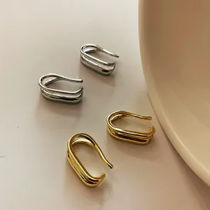 Minimalistische zweilagige gold-silberne Ohrmanschetten auf beigeem Hintergrund