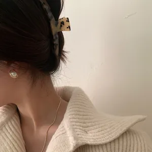 Close-up of tortoise shell acetate hair claw with pearl earrings and gold snake chain