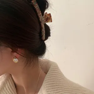 Detail of tortoise shell hair claw clip and pearl earrings worn by a model