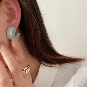 Dettaglio di orecchini grigi a C e anelli d'oro a strati su una modella