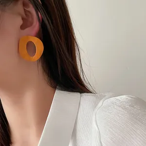 Dettaglio di un grande orecchino geometrico in legno arancione indossato da una modella.