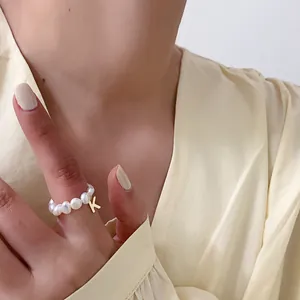 Elegante parelring met gouden letter K-hanger gedragen aan de wijsvinger bij zacht licht
