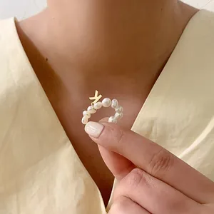 Detailopname van een parelring met een gouden letter K-hanger aan de hand gedragen