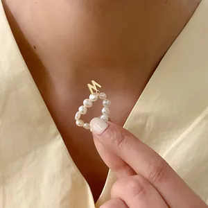 Detail van een parelring met gouden letter M hanger aan vinger, Franse retro stijl