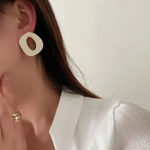 Dettaglio dell'orecchino in resina crema e anello dorato su modella in camicia di seta