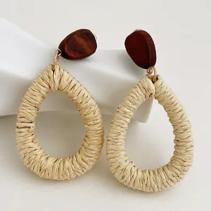 Dettaglio di orecchini a goccia in rafia intrecciata con perla in legno stile boho
