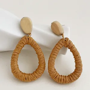 Dettaglio macro di orecchini pendenti in rattan intrecciato marrone e legno naturale