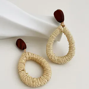 Dettaglio di orecchini boho con trama in rafia bianca e perni in legno marrone